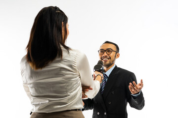 a female journalist with long brown hair standing interviewing an adult men in black suit using a black microphone
