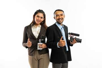 a female journalist in brown blazer and a male journalist in black suit standing together with thumbs up and smiling