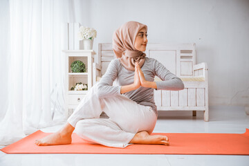 asian muslim woman instructor wearing hijab doing yoga pilates pose tutorial on orange mattress in a room