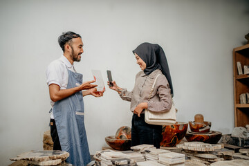 Male waiter serves female Muslim customers while scanning something for non-cash payment at a stone craft shop