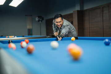 portrait of handsome asian billiard player poking the ball happily at billiard studio
