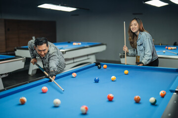 Fototapeta premium male billiard player targeting the object balll with the cue stick whiile the female player standing behind