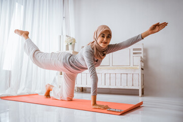 muslim woman wearing hijab t-shirt pants smiling warming up before exercise doing yoga or pilates pose on mattress in a room