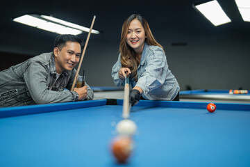 female asian player smiling while poking the ball using her stick during the billiard game