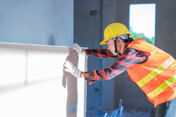 A craftsman wearing a yellow hard hat is inspecting building materials.