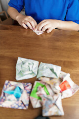 テーブルで折り紙を折る男の子の手