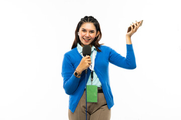 a beautiful reporter in blue shirt and blue cardigan with green name tag standing raise her left hand with her right hand bring a microphone and smiling