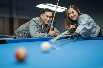 male pool player holding the glass of drink while pay serious attention to the female player that...