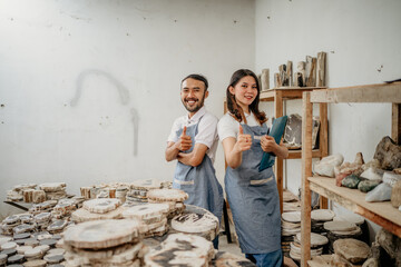 smiling young man and young woman stone craft entrepreneurs with thumbs up in a craft shop