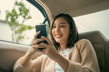 Relaxing moment of beautiful woman sitting in car back seats using smartphone play social media with safety belt and look out the window. Female happy in car traveling on the road to destination.
