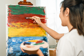 Asian woman artist working on painting with brush and variant acrylic color. Female artist painter...