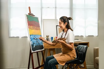 Fototapete Gemälde Asian woman artist working on painting with brush and variant acrylic color. Female artist painter on canvas in creative studio as art concept  © Chanakon