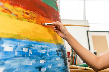 Close up hand Asian woman artist working on painting with brush and variant acrylic color. Female artist painter on canvas in creative studio as art concept