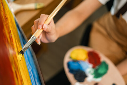 Close up hand Asian woman artist working on painting with brush and variant acrylic color. Female artist painter on canvas in creative studio as art concept