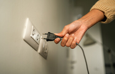 Close up woman hand put on or remove Electric plug cable in socket. Electrical equipment wires and...