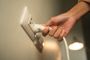 Close up woman hand put on or remove Electric plug cable in socket. Electrical equipment wires and power strips on the wall. Earth Hour saving  energy.