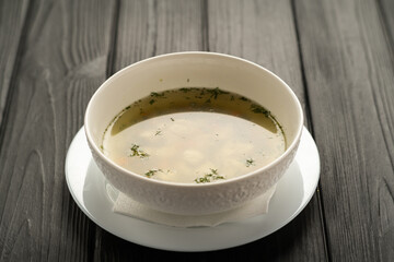 Chicken broth served in a white plate on a black wooden background, diet menu