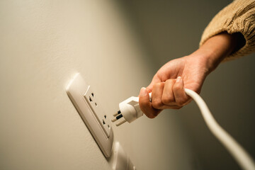Close up woman hand put on or remove Electric plug cable in socket. Electrical equipment wires and...