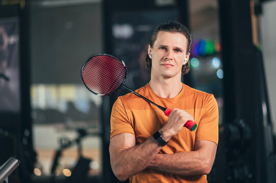 Young Caucasian trainer poses for a portrait holding a badminton racket in the gym, Young Caucasian trainer holding a badminton racket in the gym.