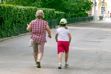 Grandmother and granddaughter walk along the sidewalk on a summer day