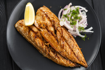 Baked mackerel fillets with lemon and onion on a black plate on dark wooden table, flat lay