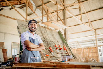 Asian male carpenter smiling with crossed hands standing in wood craft workshop