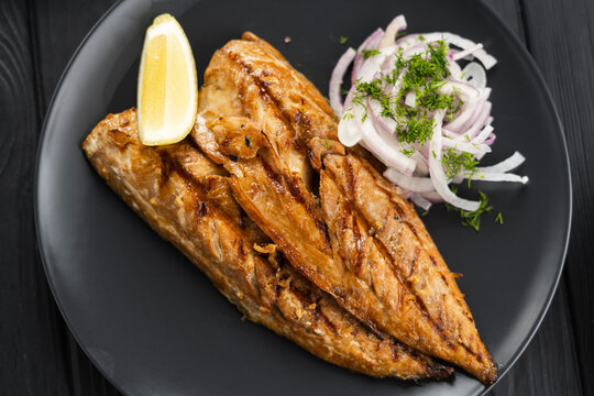 Baked mackerel fillets with lemon and onion on a black plate on dark wooden table, flat lay