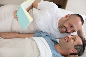 men lying on bed together while looking reading a book
