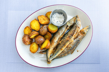 Fried smelt with boiled potatoes and mushroom sauce on a white plate. Delicious rustic lunch