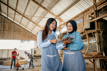 Muslim female entrepreneur working with her friend on a digital tablet in a woodcraft workshop