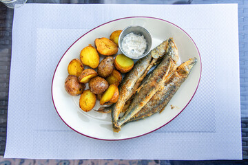 Fried smelt with boiled potatoes and mushroom sauce on a white plate. Delicious rustic lunch