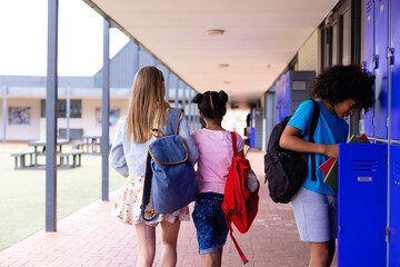 Happy diverse schoolchildren walking together in corridor at school