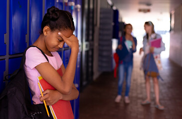 Sad african american schoolgirl standing next to lockers with diverse schoolchildren in background