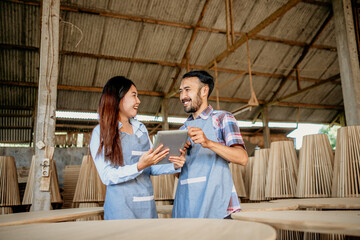 Asian enterpreneur couple chatting while working on a tablet together at a woodcraft shop