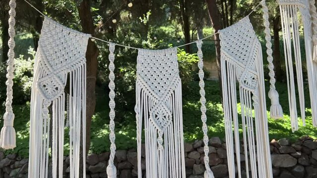 Stretching a garland of white macrame threads in a green tropical garden outdoors. Ethnic cotton decor.