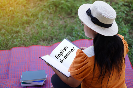 Asian woman wears white hat, sits on mat, open English Grammar book. Concept, Reading for review lesson. Education. Reading in daily life. Relax time, pastime, hobby. Give time for yourself    