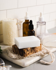 Obraz na płótnie Canvas Handmade organic bar soaps on white tile background. Sustainable zero-waste lifestyle with serum bottles and bath accessories. Copy space for your text