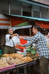 A beautiful girl wearing a headscarf selling a food stall on the side of the road gives takjil food to a buyer at the stall