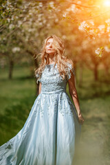 Fototapeta na wymiar Blond blooming garden. Portrait of a blonde in the park. Happy woman with long blond hair in a blue dress.