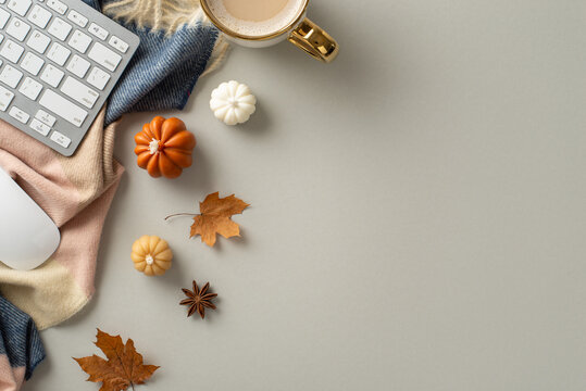 Autumn-themed workplace at home. Top view image of keyboard and mouse, gilded mug of coffee, scarf, pumpkin candles and maple foliage with space for promotion on grey isolated background
