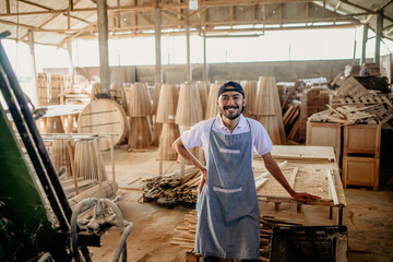 smiling male carpenter standing casually wearing an apron in a woodcraft warehouse