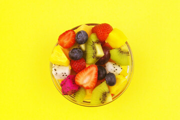 Top view of glass bowl with fruit salad on yellow background.	