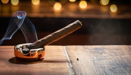  Burning handmade luxury Cuban cigar resting on an ashtray on an old wooden countertop in a nightclub or bar with copyspace © Uuganbayar