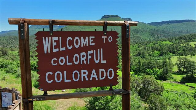 Welcome to Colorful Colorado sign. Aerial orbit revealing green Rocky Mountains in summer. State welcome sign in USA.
