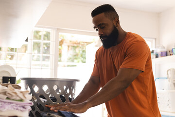 Focused african american man holding washing in kitchen with washing machine