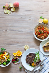 Steak, salad, noodles and other food on the table