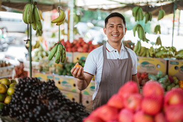 male seller smiling while holding the mandarin fruit at the fruit shop