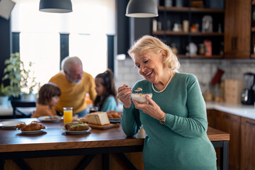 Portrait of beautiful smiling elderly woman enjoying eating muesli for breakfast with family at home. Photo with selective focus.