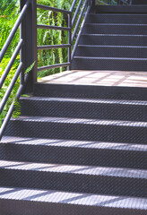 Sunlight and shadow on black metal staircase of natural skywalk in the garden at public park