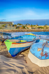 Fototapeta na wymiar Line of Dried and Moored Fishing Boats Turned Upside Down on Shore of Beach in Maspalomas at Gran Canaria in Spain